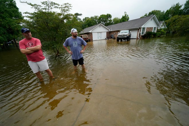 Danny Gonzales, right, stands in front of his flooded house with his neighbor Bob Neal, upset with power company trucks driving though the flooded neighborhood pushing water back into his home, after Tropical Storm Claudette passed through, in Slidell, La., Saturday, June 19, 2021.