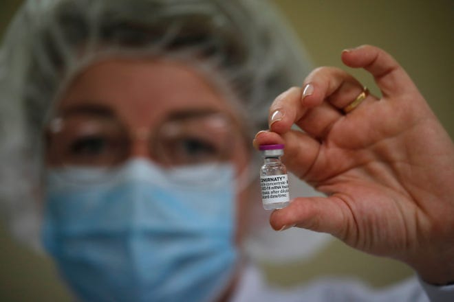 An employee holds a vial of COVID-19 vaccine in the Delpharm plant in Saint-Remy-sur-Avre, west of Paris, on Friday, April 9, 2021.