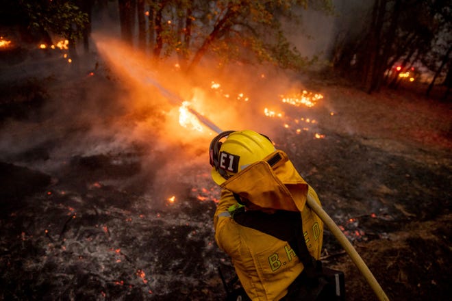 A firefighter hoses down flames from the Dixie Fire in Genesee, Calif., on Saturday, Aug. 21, 2021.