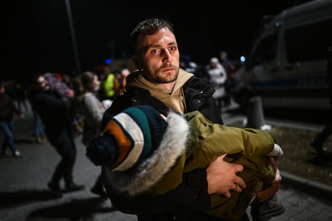 PRZEMYSL, POLAND - FEBRUARY 25: A man holds a sleeping baby after arriving by bus to a supermarket parking lot from the Polish-Ukrainian border crossing on February 25, 2022 in Przemysl, Poland. The Ukrainian government issued an order to stop 18-60 year-old men eligible for military conscription from crossing borders.